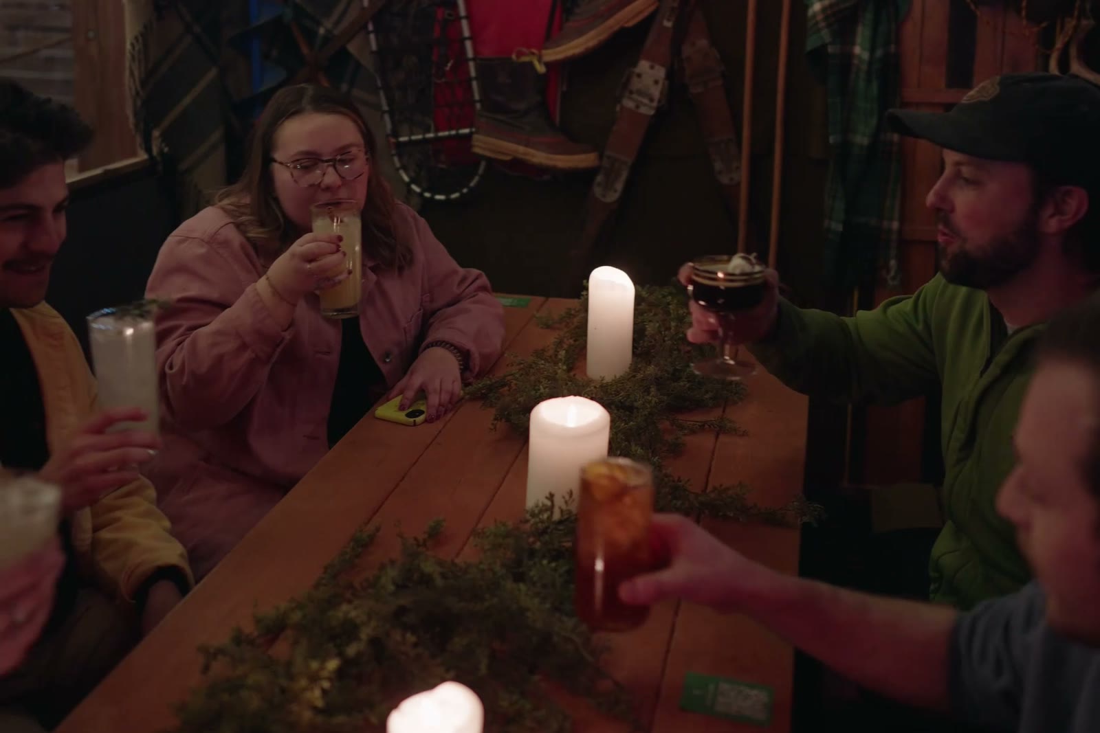 Four people raising drinks around a candlelit table inside a heated hut, string lights overhead